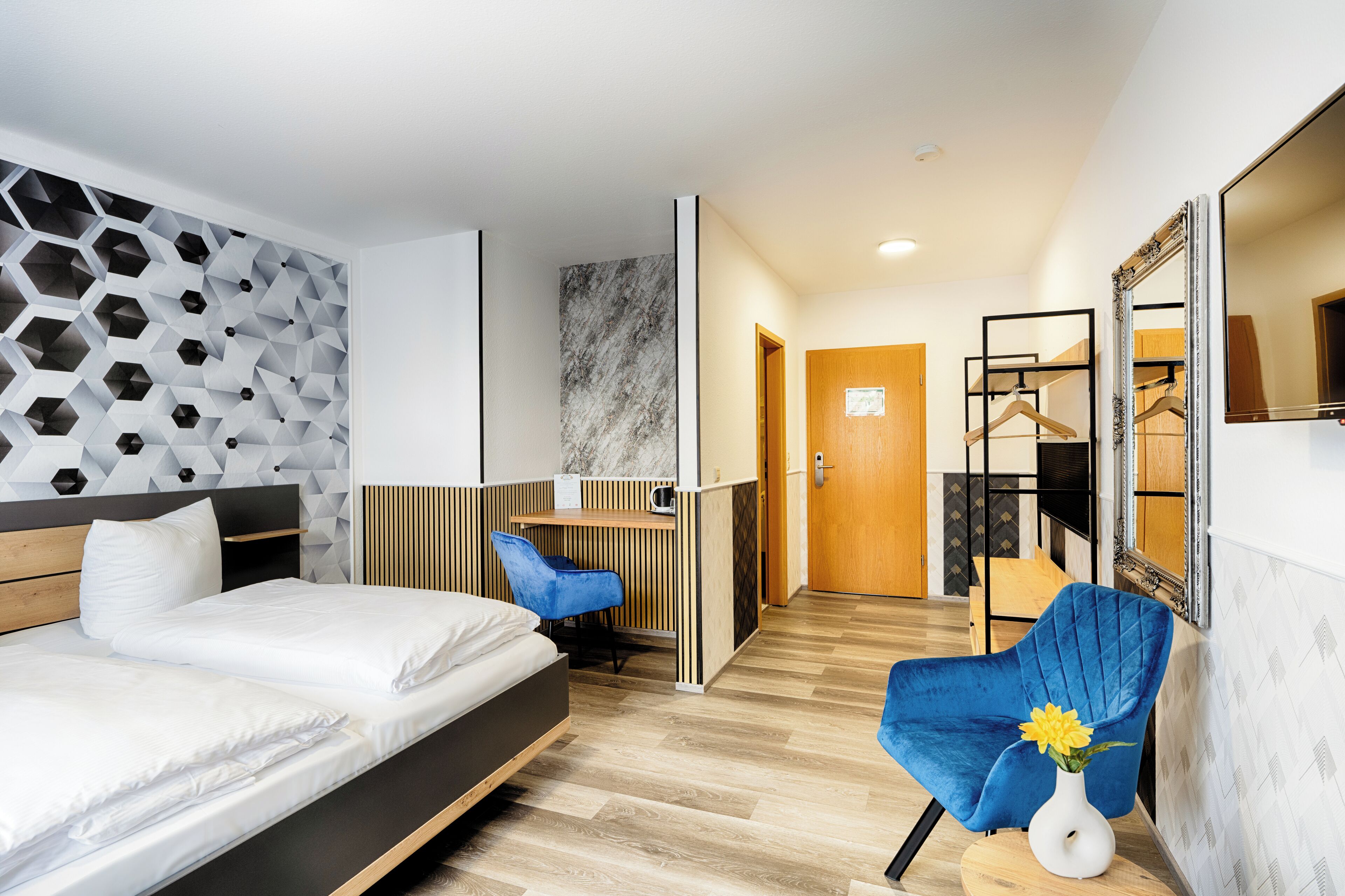 Una habitación de hotel moderna con una cama, un escritorio, una silla azul y un espejo.