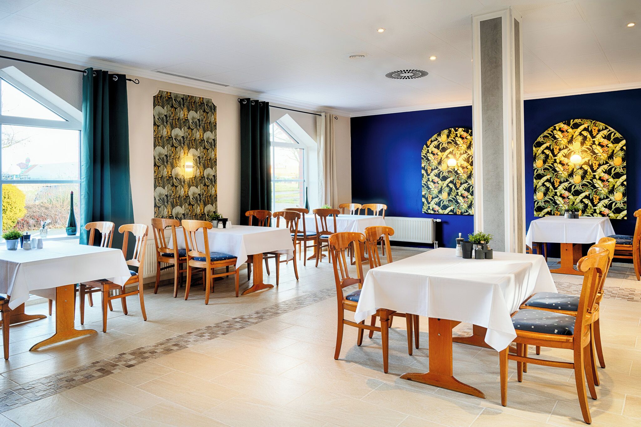 A dining area with multiple tables and chairs, large windows, and decorative wall panels.