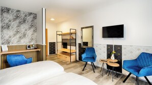 A hotel room with a bed, a desk with a computer, a chair, a TV, and a small table with a vase. - Hotel Apfelblüte (Wendorf)
