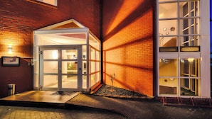 A building with a glass entrance, a brick exterior, and a small garden area. - Hotel Apfelblüte (Wendorf)