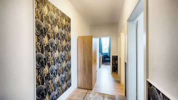 A hallway with a patterned wallpaper, a wooden door, and a rug leading to a room with a blue chair and a desk.