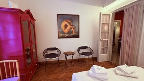 A hotel room with a wooden floor, a bed with white linens, a red cabinet, two black chairs, a small round table, and a painting on the wall. - Casa Magnolia- Big apartment near the Arena (Verona)