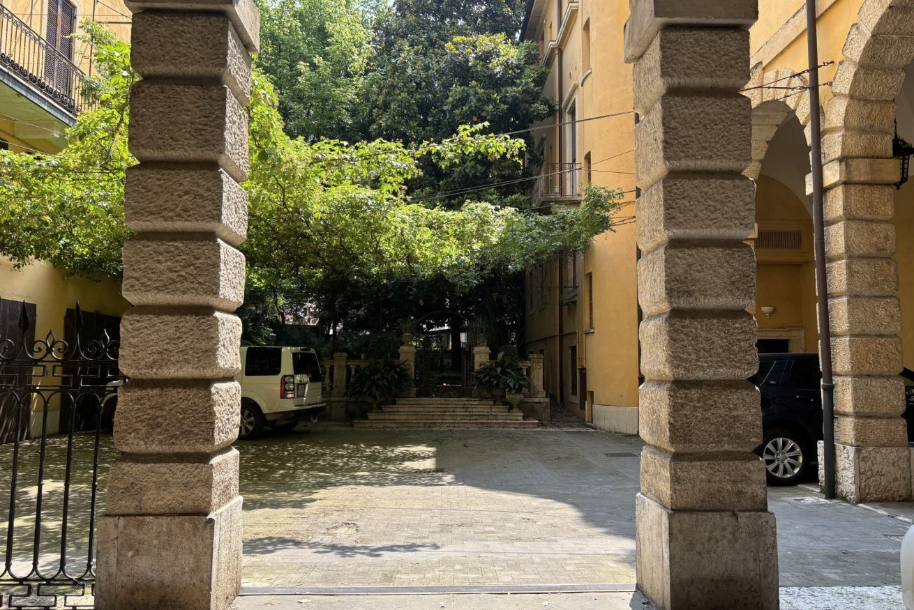 A courtyard with stone columns, a paved path, and a vehicle parked in the background.