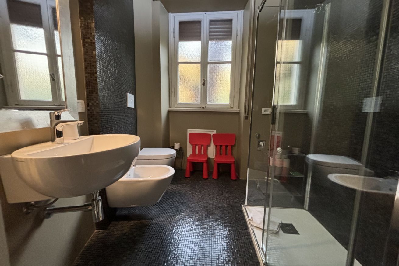 A bathroom with a large white sink, a toilet, a shower area, and a window with frosted glass.