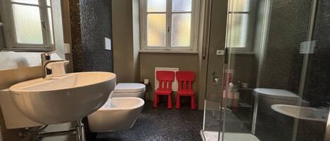 A bathroom with a large white sink, a toilet, a shower area, and a window with frosted glass.