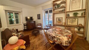 A living room with a wooden herringbone floor, a brown sofa, a coffee table, a dining table with a quilt, and a bookshelf with framed pictures and books. - Casa Magnolia- Big apartment near the Arena (Verona)