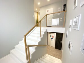 A staircase with white steps and wooden handrails, leading to a room with a black brick wall and a door with a sign. - Pensjonat Borek (Medyka)