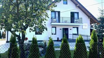 Ein zweistöckiges Haus mit Balkon, einem sichtbaren Schild und einem umzäunten Garten.