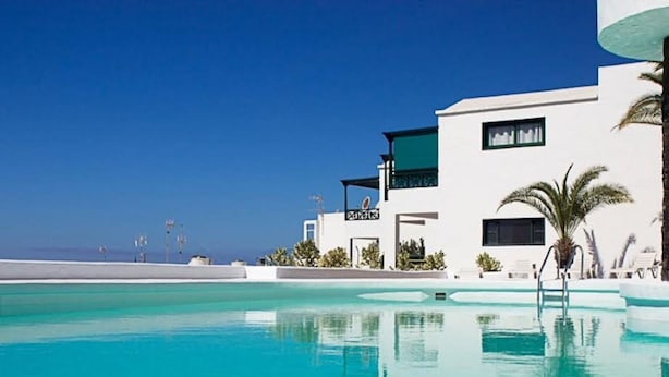 Un hotel moderno con piscina, fachada blanca y palmeras.