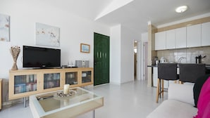 Una sala de estar moderna con una mesa de centro de vidrio, un televisor de pantalla plana y un mueble de madera.