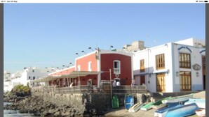 Un edificio costero con fachada roja, una pared de piedra y un muelle con barcos.