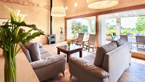 A spacious living area with a fireplace, comfortable seating, and large windows offering a view of the outdoors. - Mallorcan charm with countryside views and pool (Son Servera)