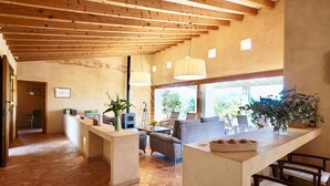 A spacious living area with a high ceiling, wooden beams, a central seating area with sofas, a coffee table, and a TV. There are potted plants and a large window providing natural light. - Mallorcan charm with countryside views and pool (Son Servera)