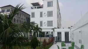 A courtyard with a white building, green chairs, and palm trees. - Perfect Havens at Platinum 5 (Lagos)