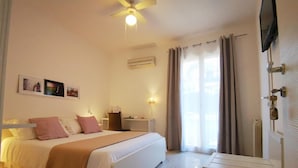 Une chambre d’hôtel comprenant un lit, des tables de chevet, un bureau, une chaise, un ventilateur de plafond, un appareil de climatisation, un téléviseur fixé au mur et une fenêtre avec des rideaux.