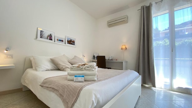 Une chambre d’hôtel moderne avec un lit soigneusement fait, un bureau avec une lampe et une vue dégagée sur l’extérieur grâce à une grande fenêtre.