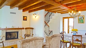A dining area with a fireplace, wooden chairs, a table with a lace tablecloth, and a chandelier.