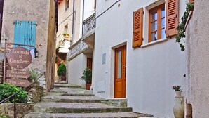 A narrow stone staircase leading to a building with a wooden door and shutters. There is a sign indicating a traditional restaurant and a view of a lake.