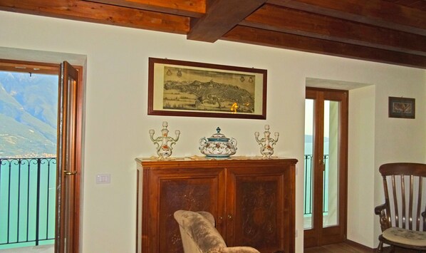 A room with a wooden cabinet, a framed landscape painting, and a view of mountains through a balcony door.