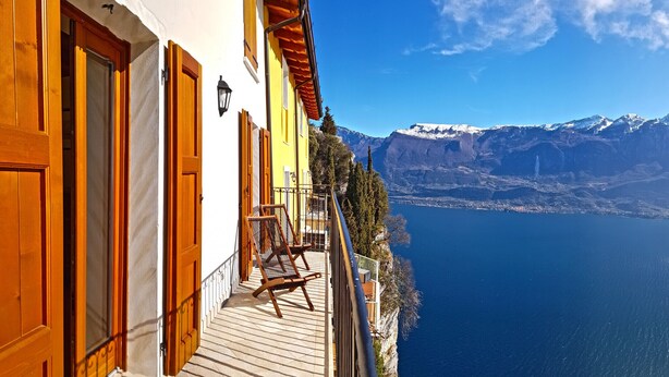 A balcony with a chair, overlooking a calm sea and snow-capped mountains.