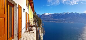 A balcony with a chair, overlooking a calm sea and snow-capped mountains.