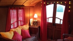 Una stanza accogliente con una panca in legno, tende rosse, un tavolo con una lampada e vista dalla finestra.