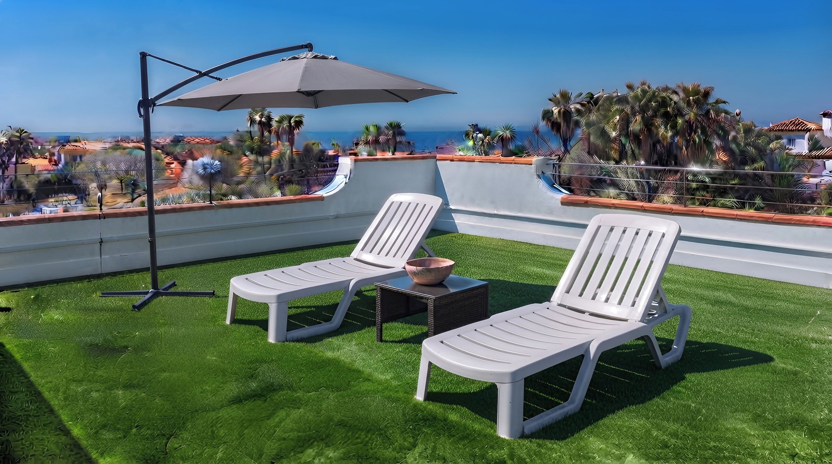 A rooftop terrace with two white lounge chairs, a small table, and a large umbrella.