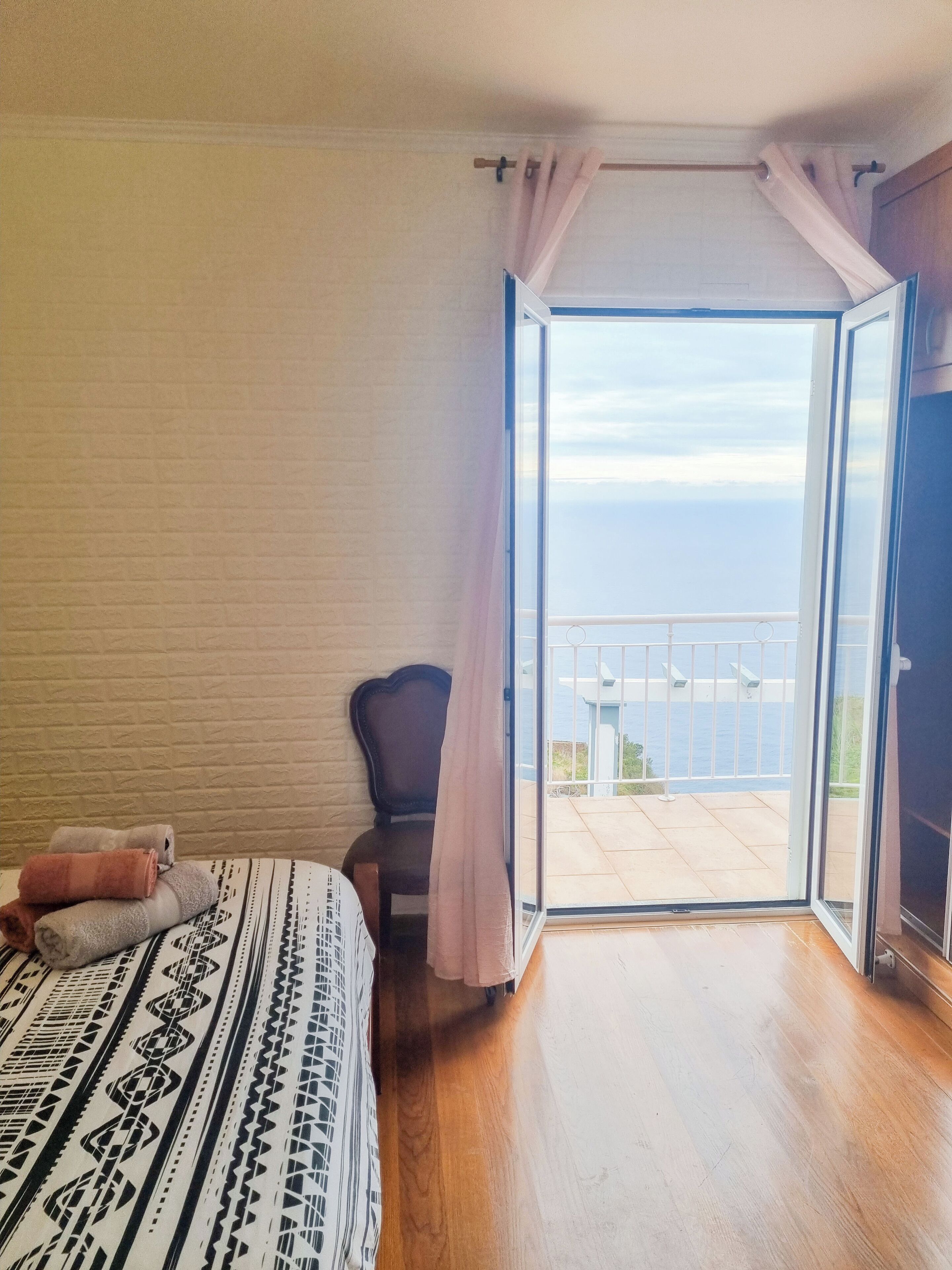 Un dormitorio con cama, una silla y vista al mar a través de una puerta abierta.