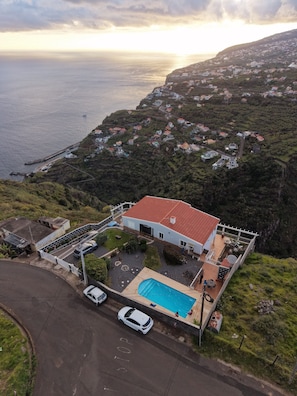 Ein Küstenhaus mit Swimmingpool, umgeben von viel Grün und Blick auf das Meer.