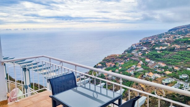 Ein Balkon mit Tisch und Stühlen mit Blick auf eine Küstenstadt und das Meer.