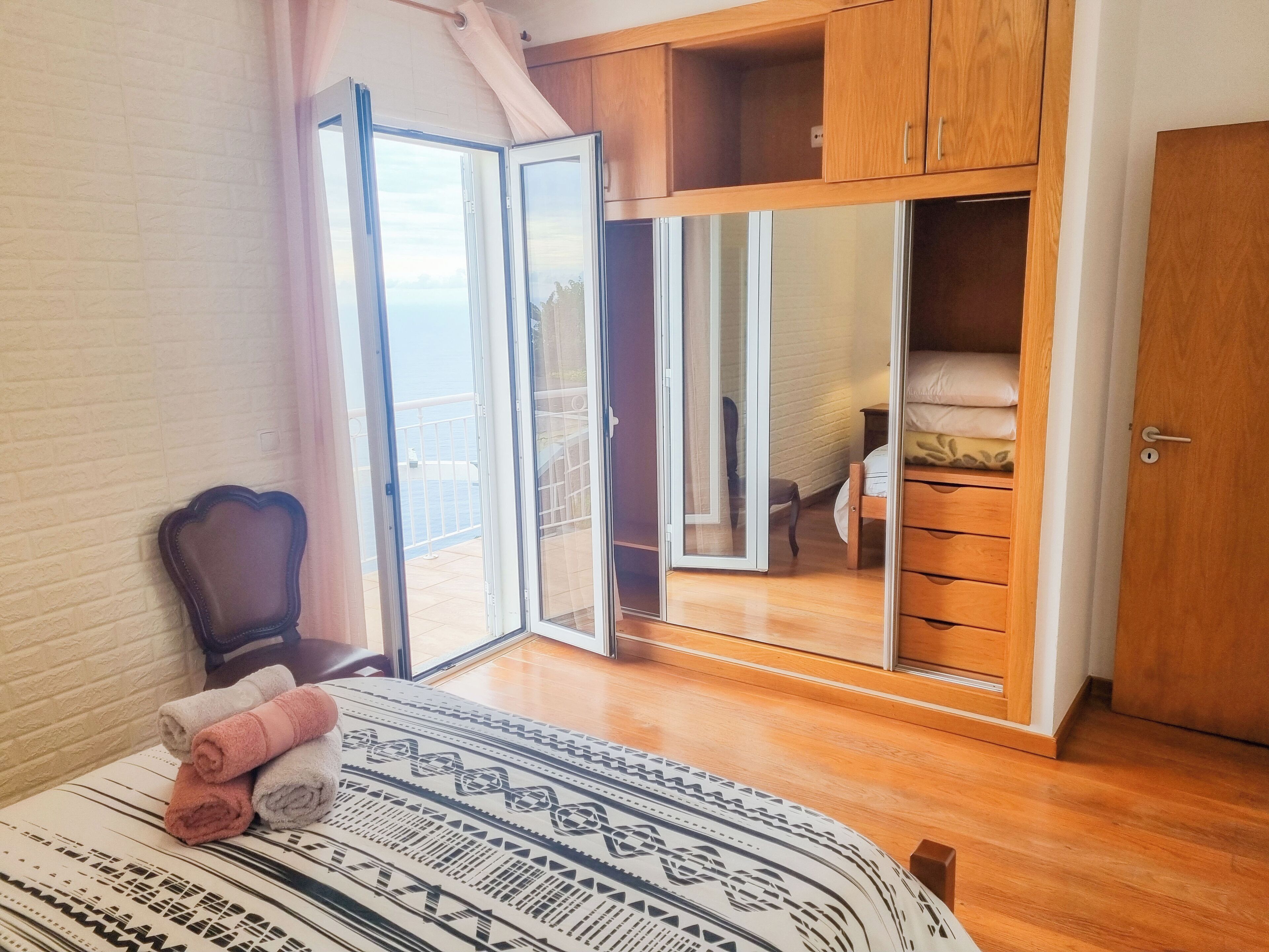 Een slaapkamer met een bed, een stoel, een kledingkast en een glazen schuifdeur die leidt naar een balkon.