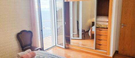 Ein Schlafzimmer mit Bett, Stuhl, Kleiderschrank und einer Schiebetür zum Balkon.