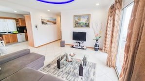 Ein modernes Wohnzimmer mit einer Couch, einem Couchtisch, einem Flachbildfernseher und einem Essbereich, im Hintergrund eine Küche.