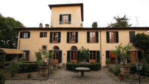 Edifici de dues plantes amb un pati interior, que presenta una zona central d'seients, diverses finestres amb persianes i vegetació al voltant.