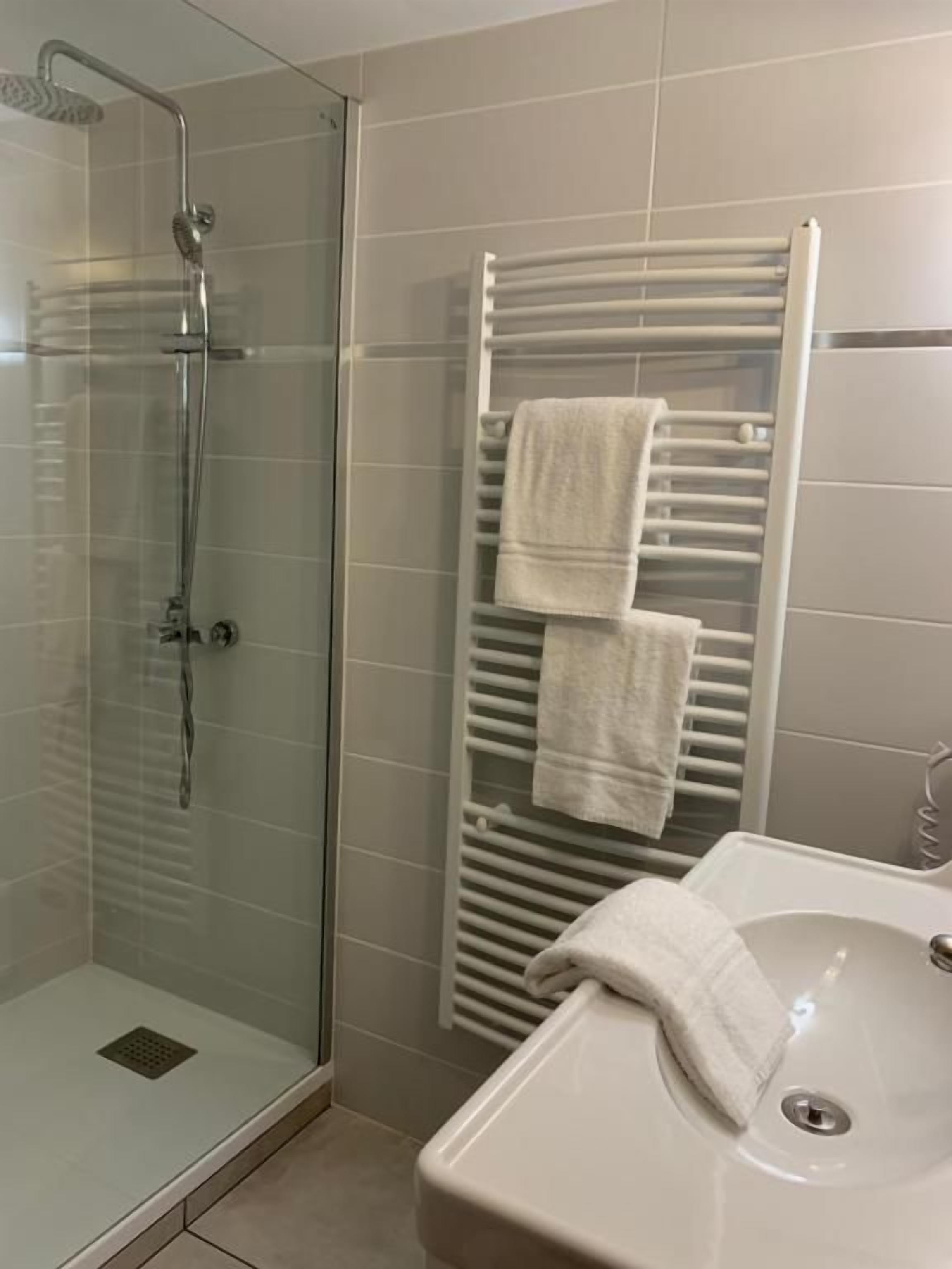 Un baño con ducha de vidrio, un perchero con dos toallas y un lavamanos.