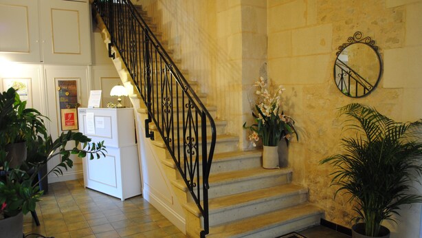 A staircase with a black iron railing, a welcome mat, and potted plants. - Auberge du Porche (Blaye)