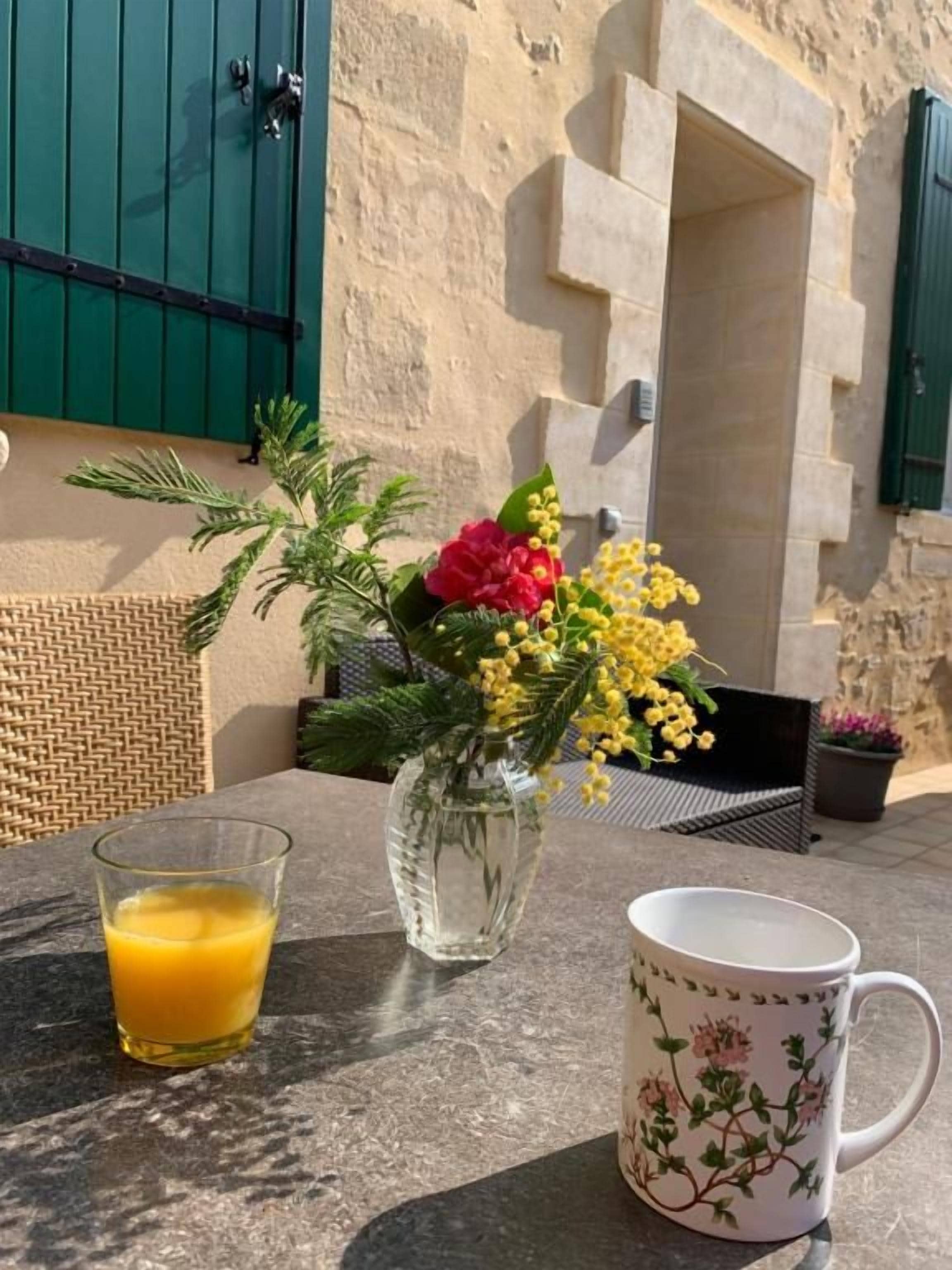 Une table avec un verre de jus d’orange, un vase de fleurs et une tasse.