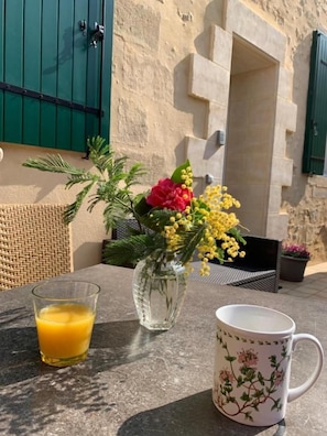 A table with a glass of orange juice, a vase with flowers, and a mug. - Auberge du Porche (Blaye)
