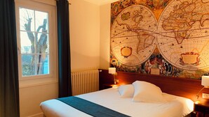 A hotel room with a large bed, a window with curtains, a wall map, and a nightstand with a lamp. - Auberge du Porche (Blaye)