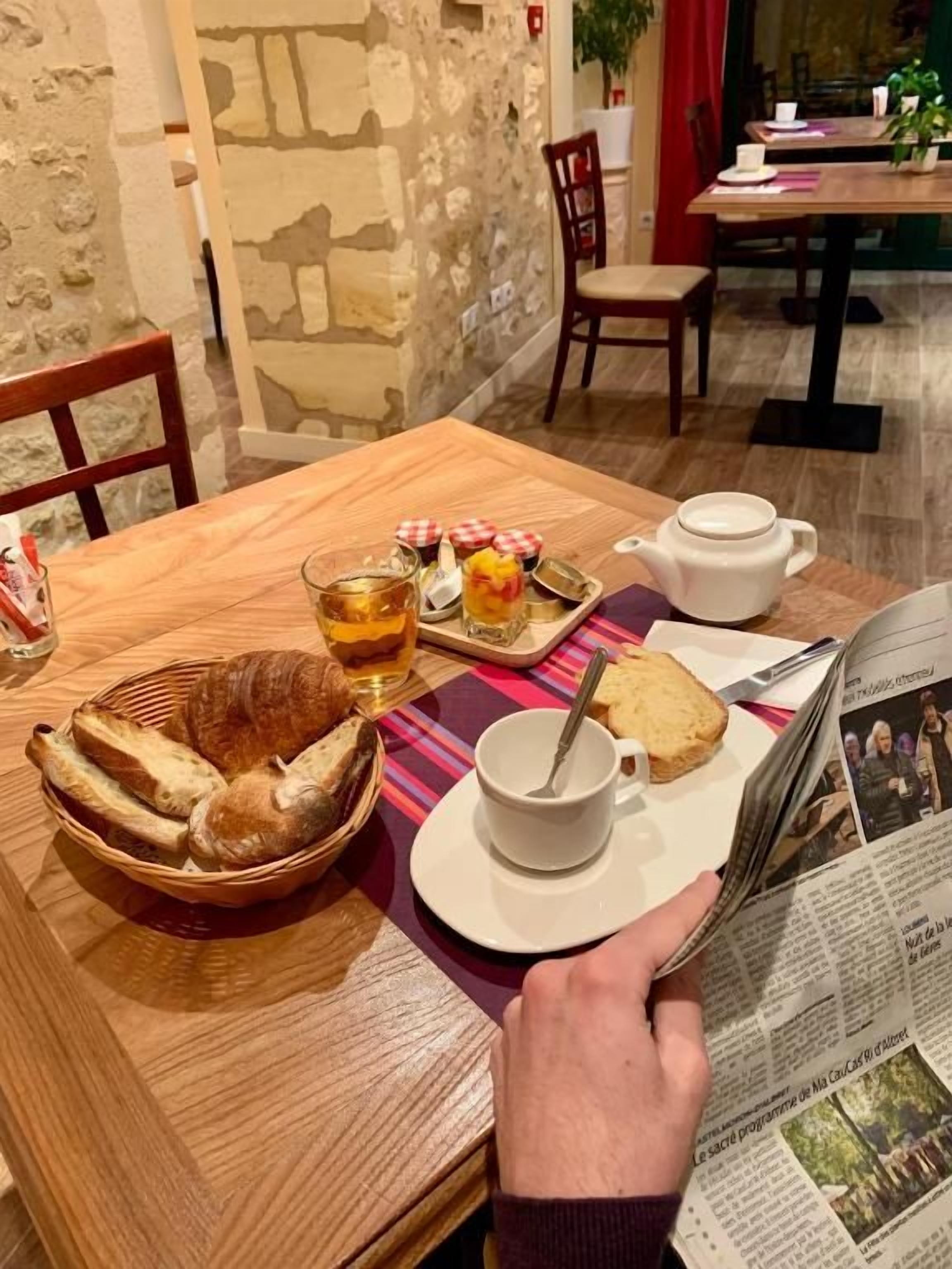 A breakfast setting with bread, tea, and a newspaper on a wooden table.
