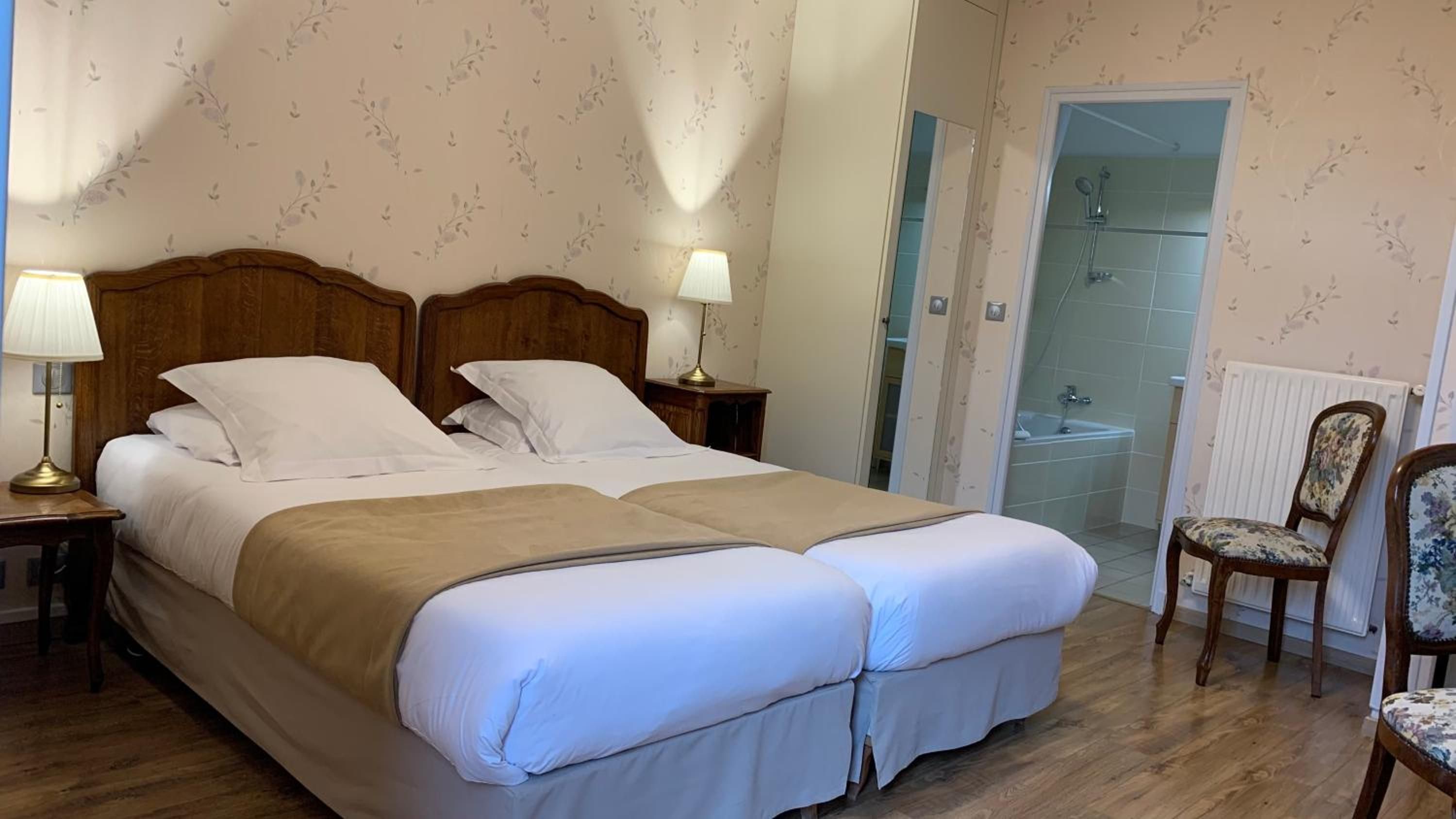 A double bed with a wooden headboard, two bedside tables with lamps, a chair, and a shower area.