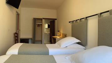 Habitación de hotel con dos camas, un televisor montado en la pared y un baño visible a través de una puerta abierta.