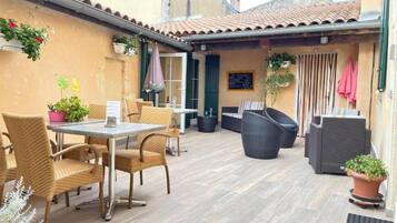 Ein Außenbereich mit einer Terrasse, Korbmöbeln, einem Tisch und Blumentöpfen.