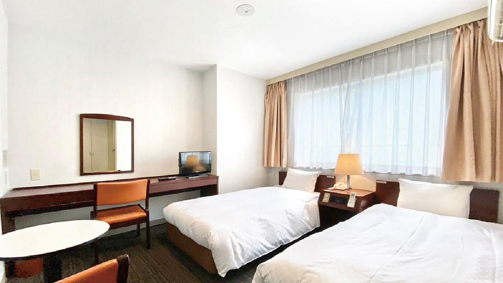 A hotel room with two beds, a desk with a chair, a television, and a window with curtains.