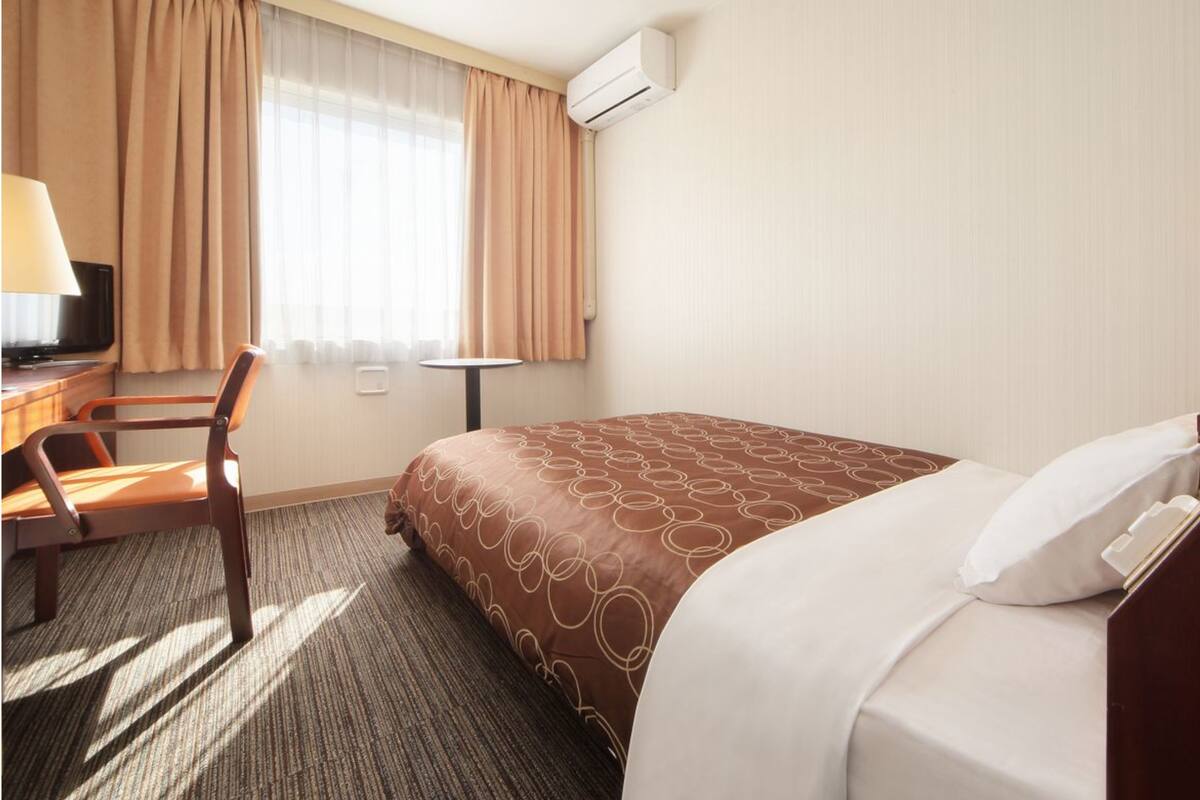 Ein Hotelzimmer mit einem Bett, einem Schreibtisch, einem Stuhl, einem kleinen Tisch und einer Klimaanlage.