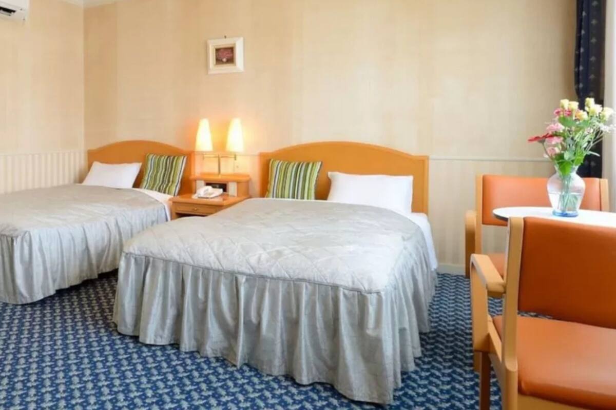 Ein Hotelzimmer mit zwei Betten, einem kleinen Tisch mit Blumenvase, einem Stuhl und einem Spiegel.