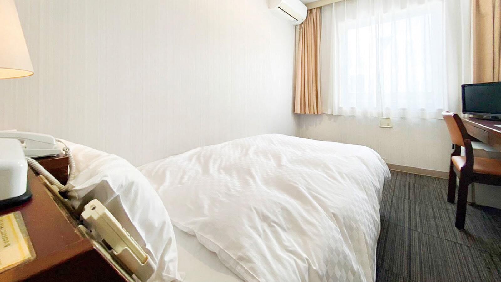 A hotel room with a bed, a desk with a computer, a telephone, and a window with curtains.