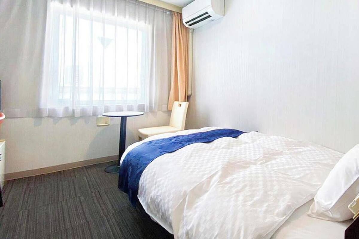Ein Hotelzimmer mit einem Bett, einem Sessel, einem kleinen Tisch, einer Klimaanlage und einem Vorhangfenster.
