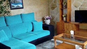 Ein Wohnzimmer mit einem petrolfarbenen Sofa, einem Holztisch und einer Steinwand.