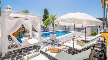 Un espace aménagé au bord de la piscine, avec des chaises longues, des parasols et une piscine.